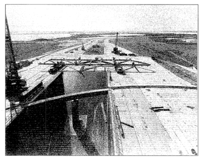 Small-format photograph: The RSS Bottom Truss Weldment, 160 feet in length, delivered to the Pad Deck at Space Shuttle Launch Complex 39-A, immediately south of the Flame Trench, which it spanned during erection, prior to being lifted into place.